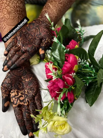 A rich, dark henna stain on both hands, beautifully accessorized with flowers. This shows how my mehendi can be the perfect centerpiece for your festive or wedding guest look.