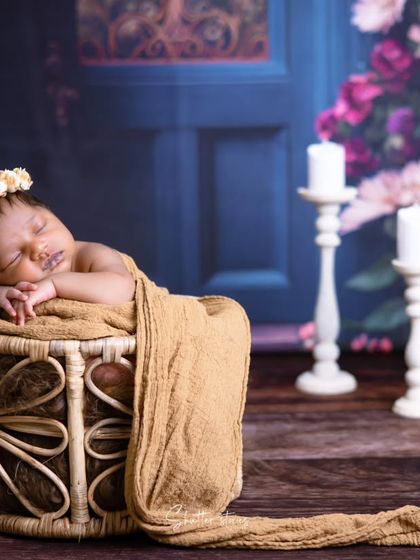 A dreamy and romantic setup with a newborn sleeping in a rattan basket against a floral backdrop with candles.