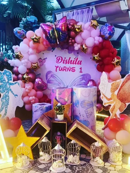 A beautiful butterfly and fairy themed decoration for a first birthday. I used a pink and purple balloon arch, glittery fairy cutouts, and decorative bird cages to create a magical setting.
