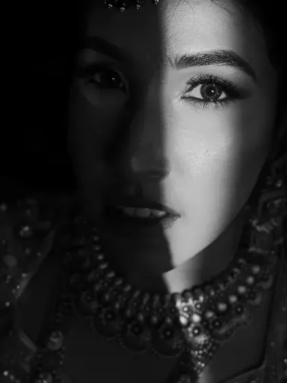 A dramatic black and white close-up of the bride's face, with a strong play of light and shadow creating a powerful portrait.