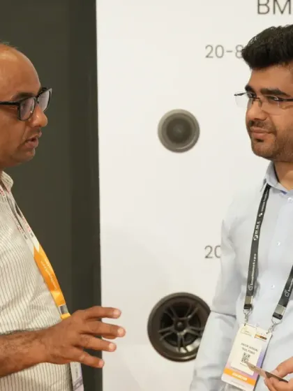 Two industry professionals discuss audio technology next to a display of in-wall speakers. The expo is the ideal place to explore specialized solutions for home integration projects.