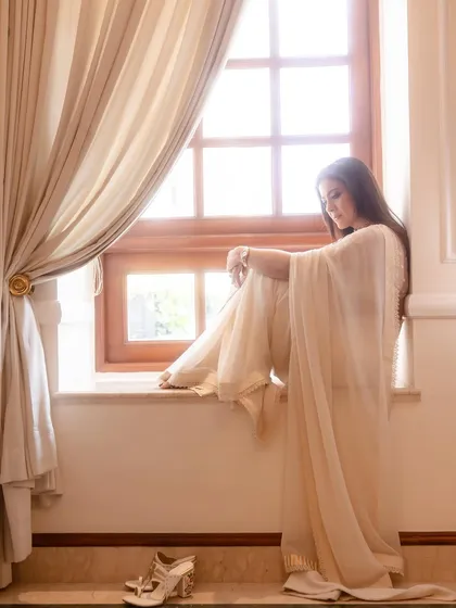 A candid shot of Kajol seated on a windowsill, showcasing the delicate hand-embroidered blouse and the beautiful heels chosen for the look.
