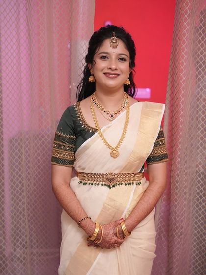 A full portrait of this bride's Muhurtham look. I ensured her makeup was perfectly balanced, with a soft lip and defined eyes, to complement her intricate jewelry and the classic white and gold saree.