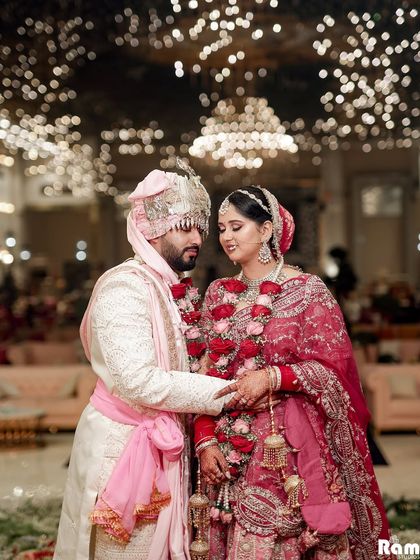 A beautiful portrait of the newly married couple under a canopy of lights, their loving gaze and coordinated pink and white outfits creating a romantic image.