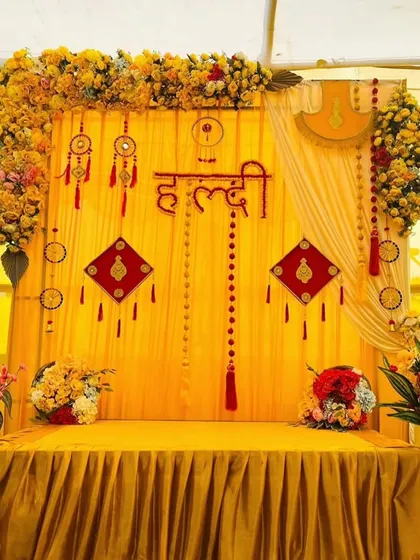 This Haldi backdrop combines traditional yellow drapes with unique decorative hangings and the auspicious 'Haldi' sign in Hindi script.