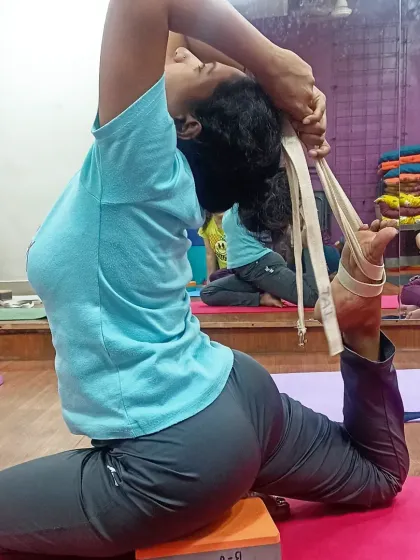 A student uses a yoga block and belt to achieve the correct alignment in Eka Pada Rajakapotasana. Props are instrumental in learning the mechanics of complex poses safely.
