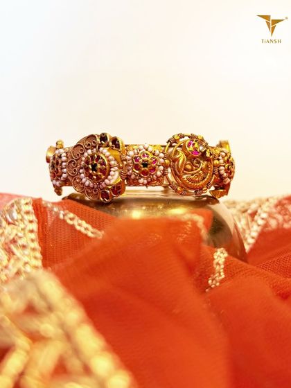 Gold that tells a story. This traditional bangle features three ornate medallions with delicate pearl borders and vibrant ruby centers. The vintage inspired craftsmanship makes this more than jewelry, it is wearable art.