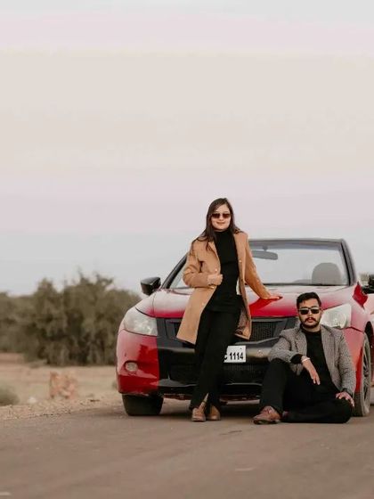 The couple poses in front of their red convertible on a quiet road, creating a chic and fashionable portrait.
