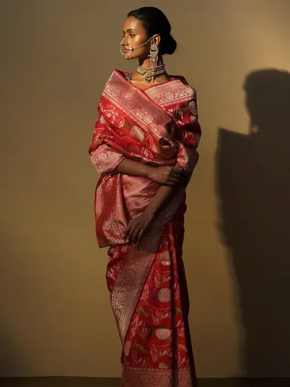 A side view of a model in a rich, red woven saree. The styling, including the traditional nose ring and choker, is designed to evoke a sense of timeless, regal beauty.