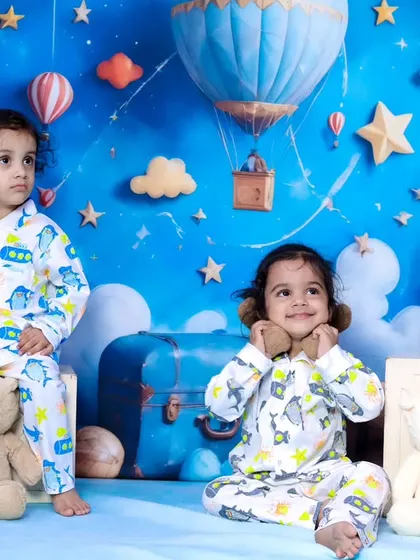 Two siblings posing together in matching pajamas, surrounded by teddy bears.