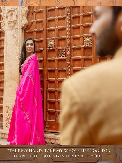 A beautifully framed shot in front of a traditional Rajasthani door. The bride's vibrant pink outfit pops against the warm tones of the sandstone, creating a visually stunning and culturally rich portrait.