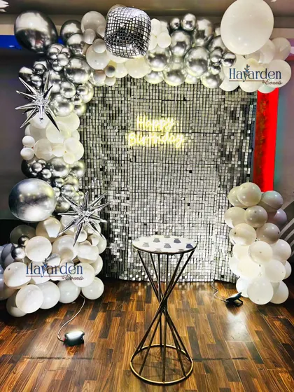 A dazzling disco-themed party with a silver sequin backdrop. The decor is accented with silver and white balloons, starburst foils, and a disco ball for that perfect retro vibe.