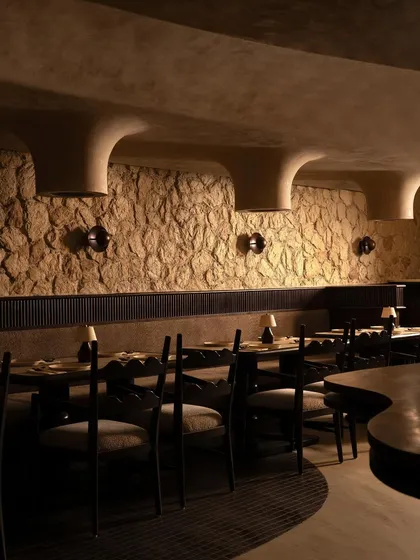 An overview of the dining space, showing how the sculpted ceiling and stone walls create a series of intimate nooks. The design encourages a personal experience of the space, with each table feeling like its own private world.
