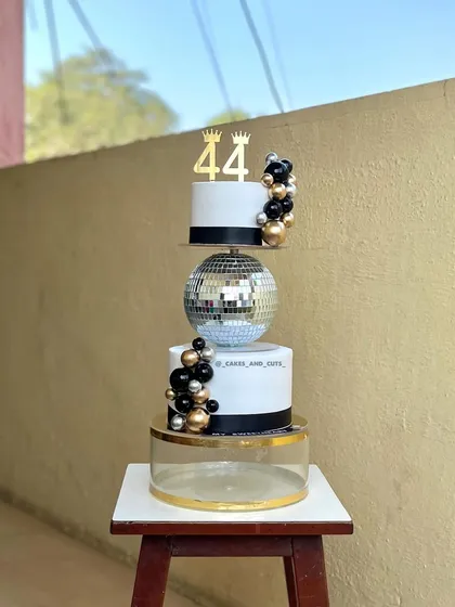 A stylish black, white, and gold tiered cake for a 44th birthday. The design includes a disco ball separator for a fun, retro party vibe.