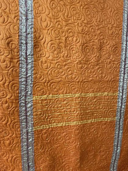 A close-up of the free-motion quilting on the orange saree quilt, highlighting the texture and preserved border.