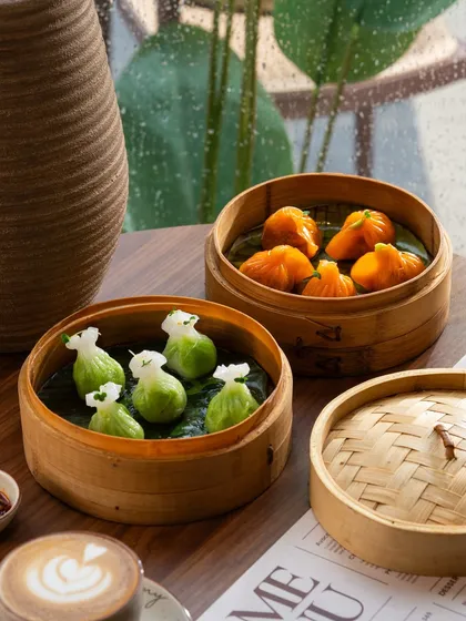 Colorful green and orange dumplings in bamboo steamers. The composition and natural light from the window create a fresh, inviting scene.