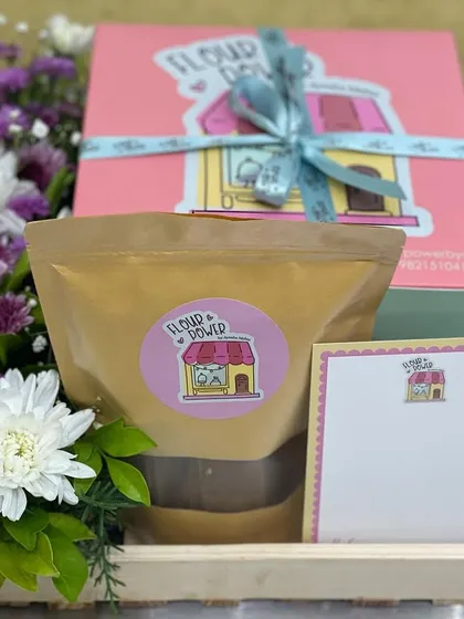 A corporate or event gifting option, this hamper includes a savoury bread, a pack of healthy snacks, and custom branded stationery, all arranged with fresh flowers in a reusable tray.