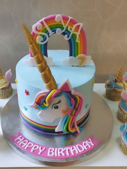 A magical unicorn-themed cake with matching cupcakes. The cake features a rainbow, clouds, and a fondant unicorn, perfect for a fantasy-filled party.