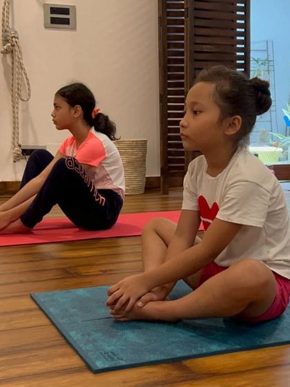 Two young girls sit with focus, ready to begin their yoga practice. Our classes enhance concentration and body awareness.