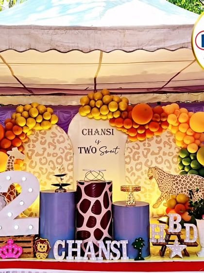 A complete jungle-themed stage for a second birthday. The setup includes a 'Two Sweet' backdrop, animal-print plinths, a large light-up number '2', and cutouts of a sheep and giraffe.