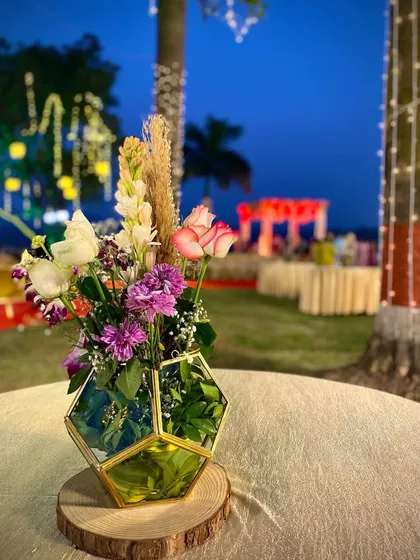 This is a modern centerpiece I made for an outdoor evening event. I used a hexagonal gold and glass terrarium vase and filled it with a mix of pink roses, purple carnations, white tuberoses, and a touch of dry pampas grass for a contemporary feel.