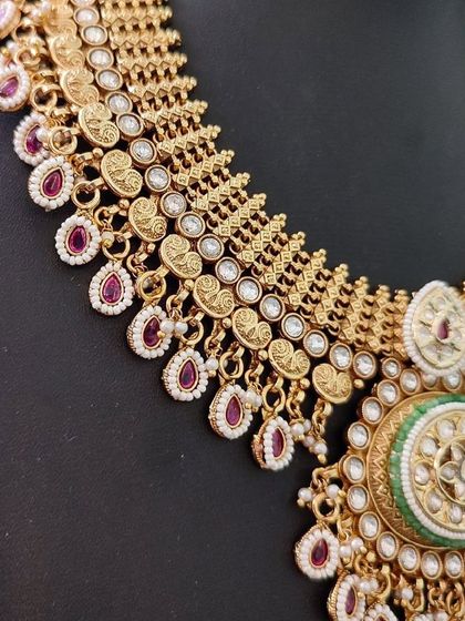 A close-up of a temple-style necklace with ruby-colored stone drops.