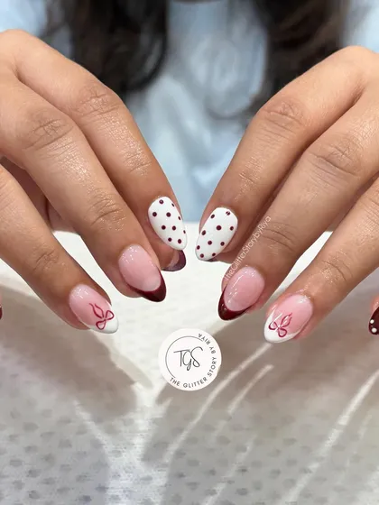 A playful mixed-and-matched set combining deep red French tips, polka dots, and delicate bow art.