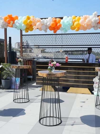 A wider view of the rooftop bar and lounge area. The open-air setting is enhanced with themed balloon decor and floral centerpieces on rustic wooden tables.
