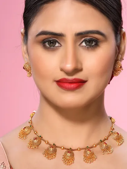 A model displays a traditional gold necklace with intricate pendant work. The simple styling ensures that the focus remains entirely on the craftsmanship of the jewellery piece.