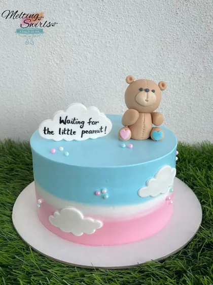 "Waiting for the little peanut!" This cute teddy bear cake is perfect for a gender-neutral baby shower. The pink and blue ombre frosting is decorated with fondant clouds and a sweet message.