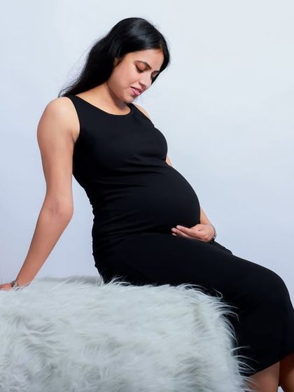 A simple and classic maternity portrait. The mother-to-be is seated in a timeless black dress against a clean white background, creating a minimalist and elegant look.