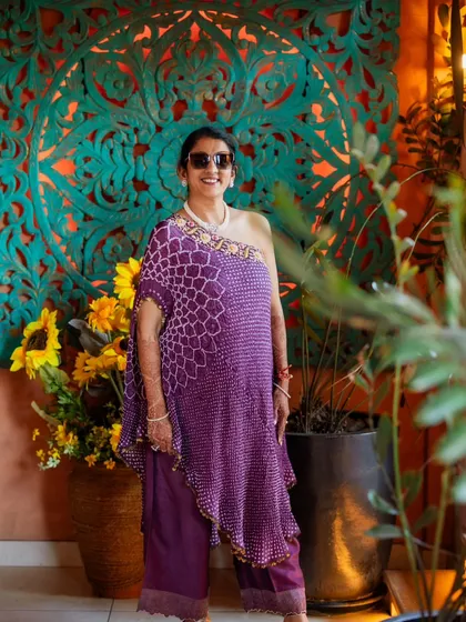 A full-length view of the mother's Haldi outfit. The asymmetrical one-shoulder bandhani top paired with matching trousers is a modern and chic take on traditional Indian textiles.