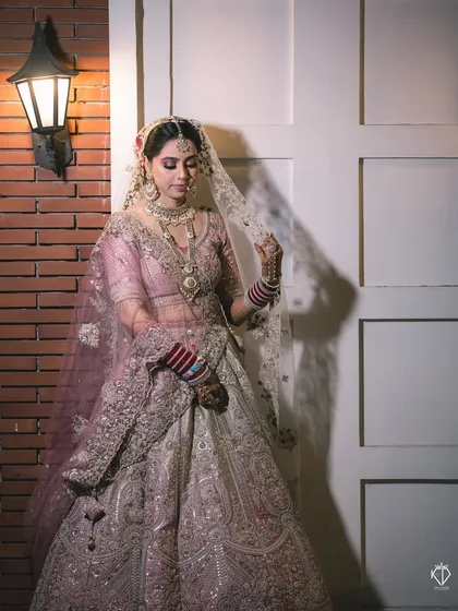 A full-length shot showing the bride in her magnificent lehenga. The soft lighting and elegant pose create a timeless portrait that feels like a painting.