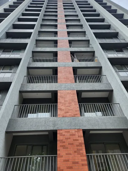 A close up of the facade at Adani Amogha, Ahmedabad. The vertical band of brick-colored tiles contrasts with the grey concrete finish, breaking the scale of the building and adding a touch of warmth to the exterior.