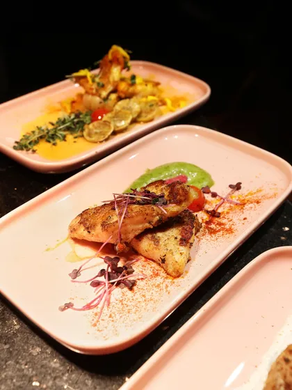 Grilled chicken with a vibrant green pea puree and microgreens. The composition on the rectangular pink plate is both modern and visually appealing.