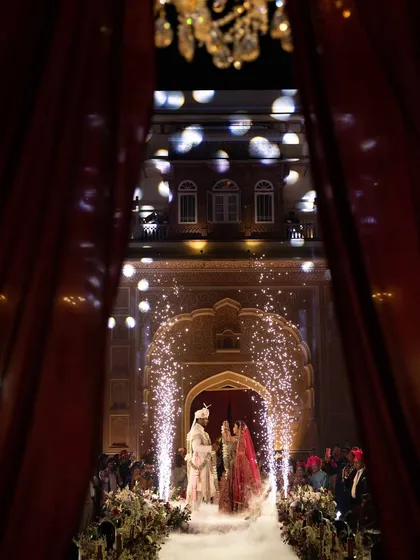 A dramatic entrance through crimson drapes reveals the couple, framed by fireworks and a path of ethereal smoke. This is how we make fairy tales a reality at heritage wedding venues.