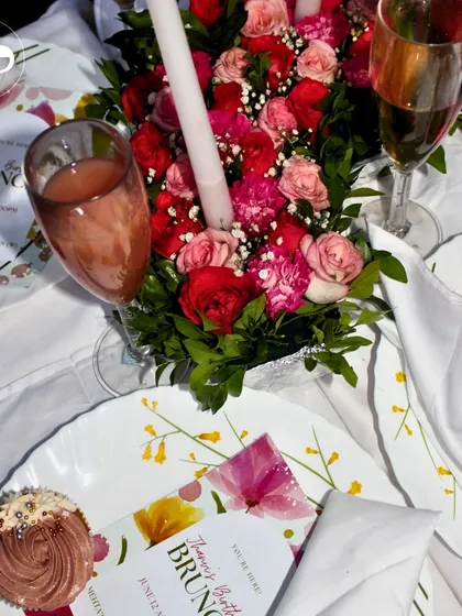 An overhead shot of a beautiful birthday brunch tablescape. The floral centerpiece, custom menus, and delicious cupcakes create a chic and celebratory setting.