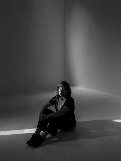 A moody black and white portrait of me, sitting in a corner with a single beam of light. It reflects the contemplative and artistic side of my work.