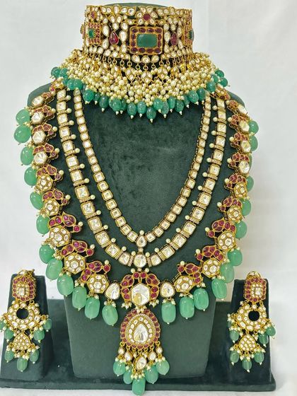 This rental bridal set combines a pearl and Kundan choker with a magnificent multi-layered necklace. The green beads and red accents add a vibrant touch.