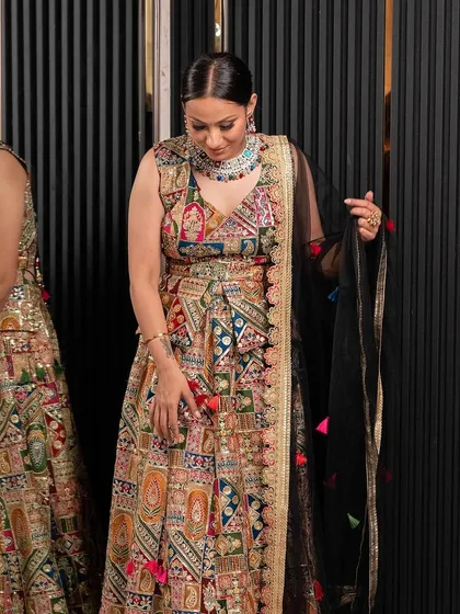A model showcasing a unique multi-colored lehenga with a black dupatta. This is a great rental for someone who loves vibrant, artistic patterns.