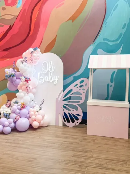 A chic and modern baby shower setup featuring a pastel butterfly theme. This highlights our attention to detail with an "Oh Baby" neon sign on an arched backdrop, a delicate balloon garland with floral inserts, and a custom butterfly wing prop.