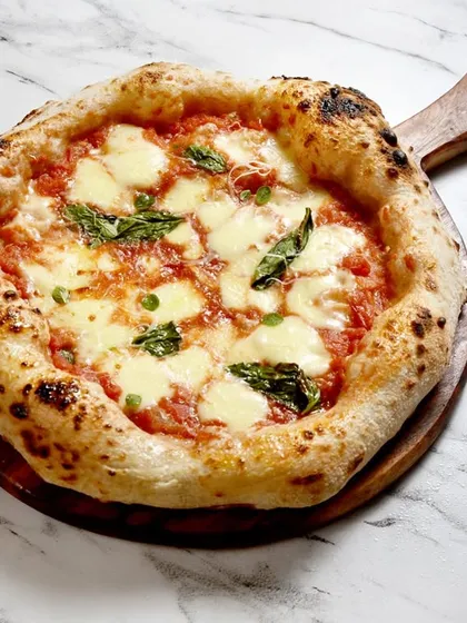 Behold, the queen of pizzas, the Margherita. This isn't just any Margherita, it's a contemporary Neapolitan style, made with authentic San Marzano tomatoes, fresh mozzarella, and basil, all on a perfectly charred, leopard-spotted crust.