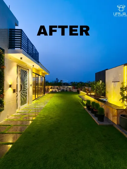 A beautiful "after" shot of a complete terrace makeover. The space now includes a lush lawn, a water feature, and a glass-enclosed room, all illuminated for a stunning evening view.