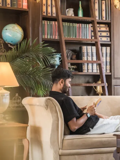 A quiet, candid moment of the groom relaxing on a couch with a book in a stately library. This solo portrait adds a personal and storytelling element to the pre-wedding collection.