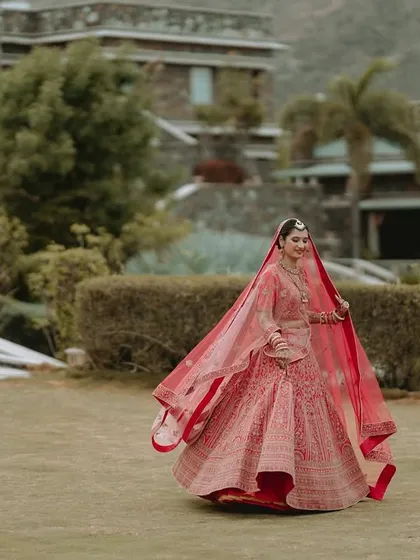 The bride twirls in her red lehenga on the lawns of the wedding venue, her veil flowing beautifully.