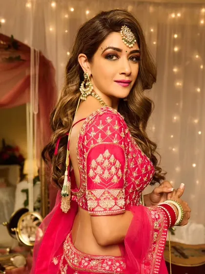 Full Hollywood glam for this bride. The look features voluminous side-swept waves, a smokey eye, and a vibrant pink lehenga, creating a stunning and memorable style for any wedding event.