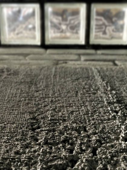 A macro shot focusing on the rough texture of a concrete wall, with glass blocks providing a smooth, translucent contrast in the background. It’s a study in how different material surfaces interact with light.