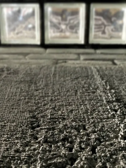 A macro shot focusing on the rough texture of a concrete wall, with glass blocks providing a smooth, translucent contrast in the background. It’s a study in how different material surfaces interact with light.