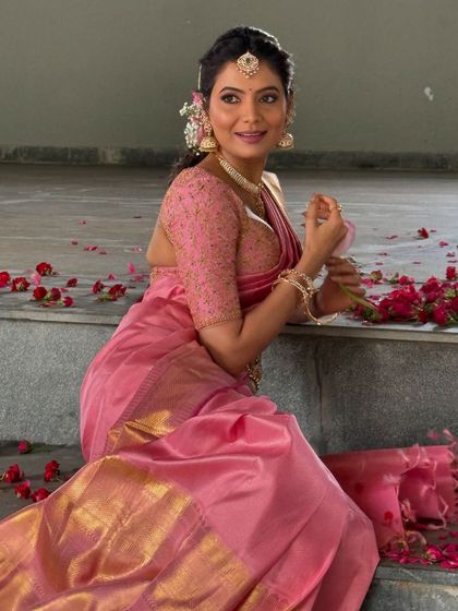 Shwetha Prasad seated amidst rose petals, looking lovely in the custom pink Kanchivaram saree and embroidered blouse.