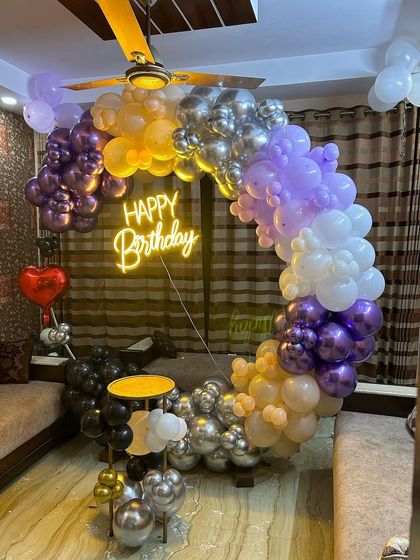 A multi-colored balloon arch for a lively birthday party at home. This setup uses a mix of chrome purple, silver, yellow, and black balloons to create a dynamic and fun look.